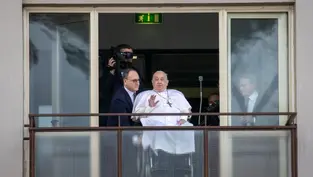 Man in white robe waving to crowd