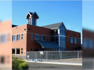 Red-brick building with large glass windows and tower against blue sky. Fenced yard in front, suggesting a secured area or campus.