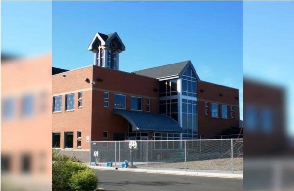 Red-brick building with large glass windows and tower against blue sky. Fenced yard in front, suggesting a secured area or campus.