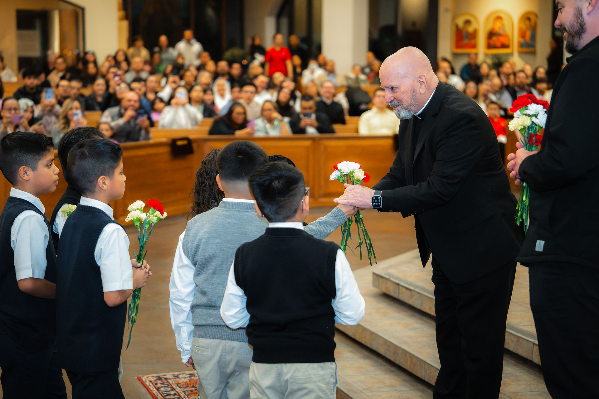 A bishop receives flowers from Catholic school students in a church. The mood is warm and celebratory.