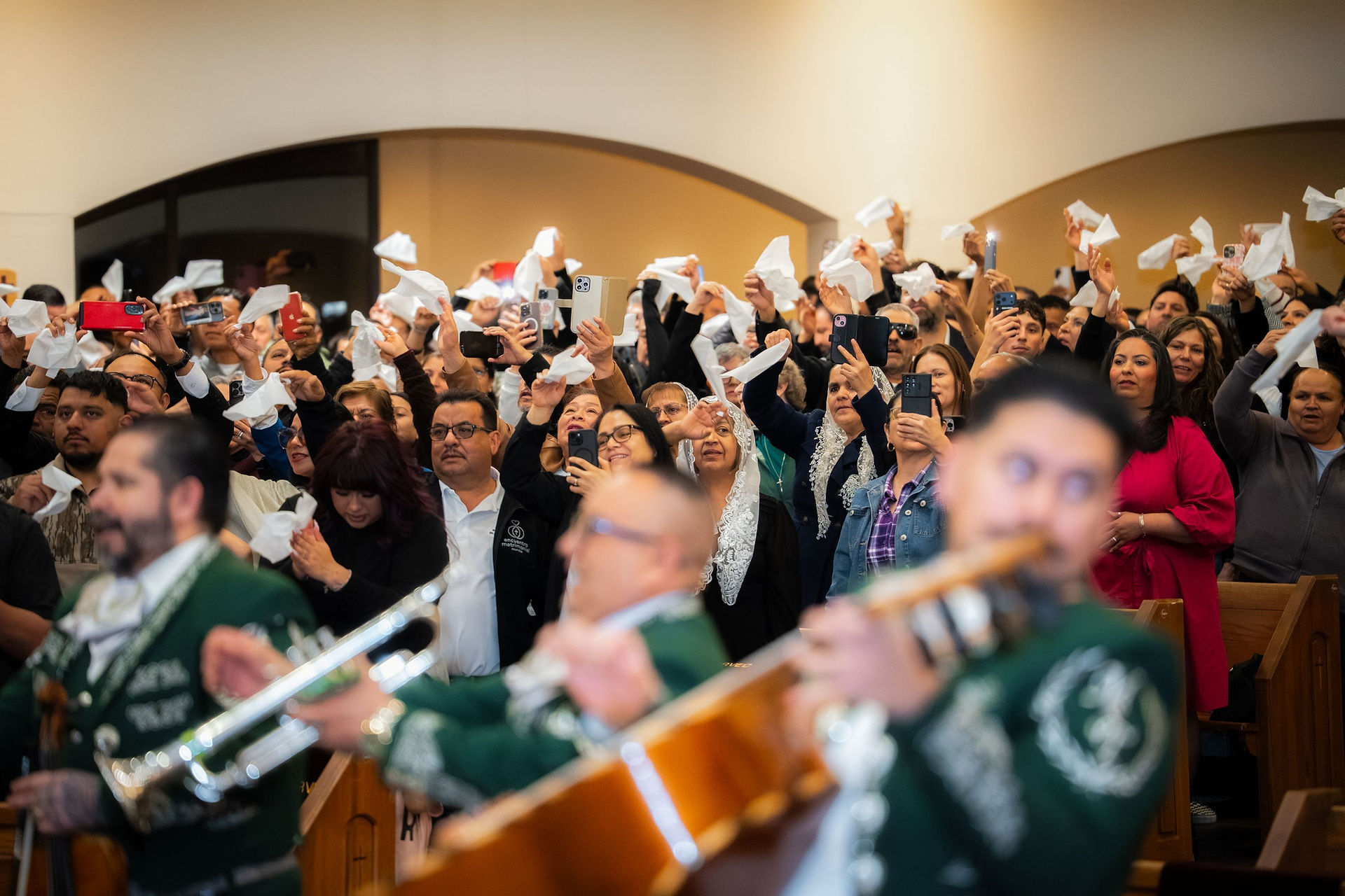 Audience in a church waves tissues and takes photos as musicians in green uniforms perform, creating a lively and joyful atmosphere.