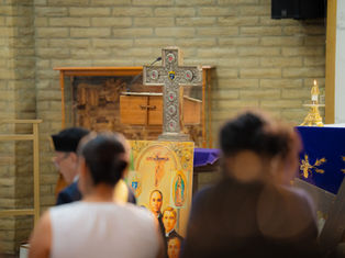 Cruz ornamentada con reliquias colocada sobre un altar en una iglesia, mientras varias personas pasan o permanecen reunidas al frente durante una ceremonia.