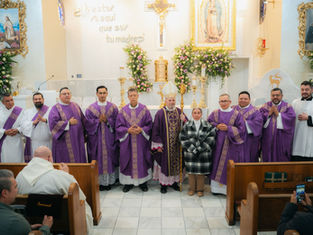 Clergy in purple vestments pose with a woman beside an altar adorned with flowers and religious artwork. Text on wall reads "Aquí que soy tu madre".
