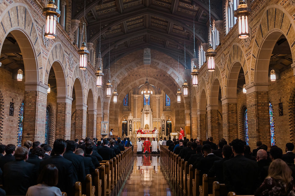 Clergy celebrate Mass at the altar of a large brick church as a full congregation sits in pews beneath arched ceilings and hanging lanterns.