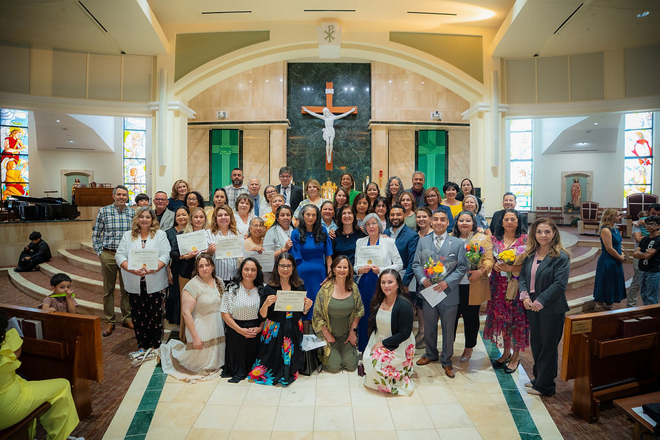Large group poses with certificates and flowers in a church before a crucifix, celebrating a joyful ceremony.