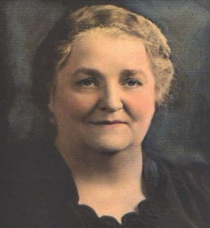 Portrait of an older woman with short wavy hair and a gentle smile, against a dark background, in a warm-toned vintage style