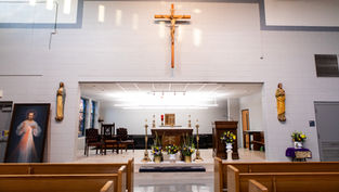 Church interior with altar, cross, and religious statues. Bright lighting, floral decorations, wooden pews, and a serene atmosphere.