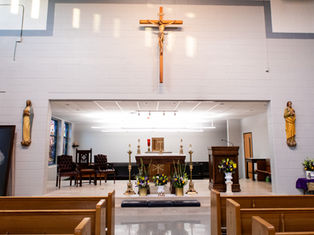 Church interior with altar, cross, and religious statues. Bright lighting, floral decorations, wooden pews, and a serene atmosphere.