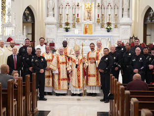 Clergy in ornate robes and police officers pose together in a decorated church with a white altar and gold accents, exuding a formal mood.
