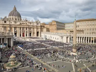 Crowd gathers in St. Peter's Square, Vatican City, under cloudy skies. The basilica and obelisk are prominent. Mood is solemn and lively.