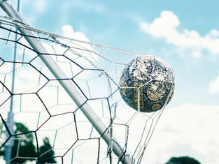 Soccer ball caught in a white net on a goal frame against a bright blue sky with clouds.