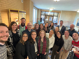 Smiling group selfie of coworkers in a brick hallway near an EXIT sign, posing closely in a bright indoor lobby