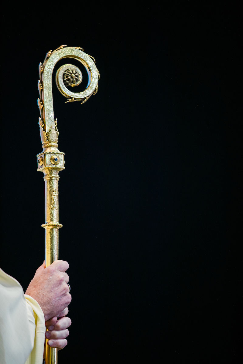 A bishop holds a crozier, symbol of his pastoral authority.