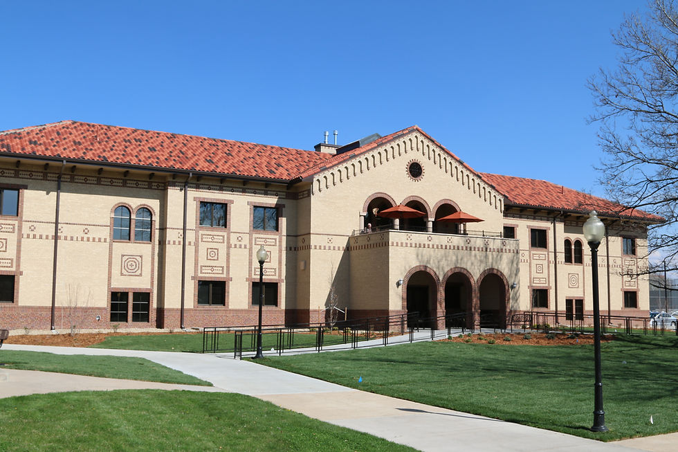 Historic building with ornate brick design and red-tiled roof under a clear blue sky. Green lawn and sidewalks in the foreground.