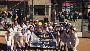 A softball team in white and purple uniforms poses with a "CHSAA State Champions Softball 2025" banner and trophy on a sunlit field.