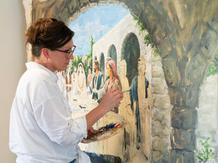 Artist in white shirt paints a detailed fresco of people under arches. Palette with vibrant colors. Focused mood. No visible text.