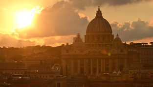 Sunset over St. Peter's Basilica in Rome. The golden sun illuminates the domed structure, with a warm glow casting over the cityscape.