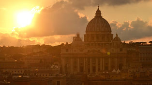 Sunset over St. Peter's Basilica in Rome. The golden sun illuminates the domed structure, with a warm glow casting over the cityscape.