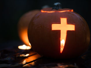 Carved pumpkin with a glowing cross cutout, lit by a candle inside. Dark background and wet surface create a moody, atmospheric scene.