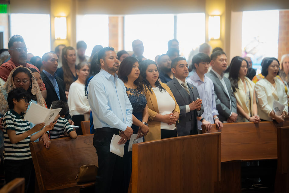Diverse congregation stands in church pews holding hymnals, facing forward in a solemn service under warm light.