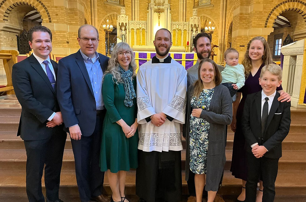 Group of people smiling in a church, one in religious robes. Stained glass and ornate architecture in the background. Celebratory mood.