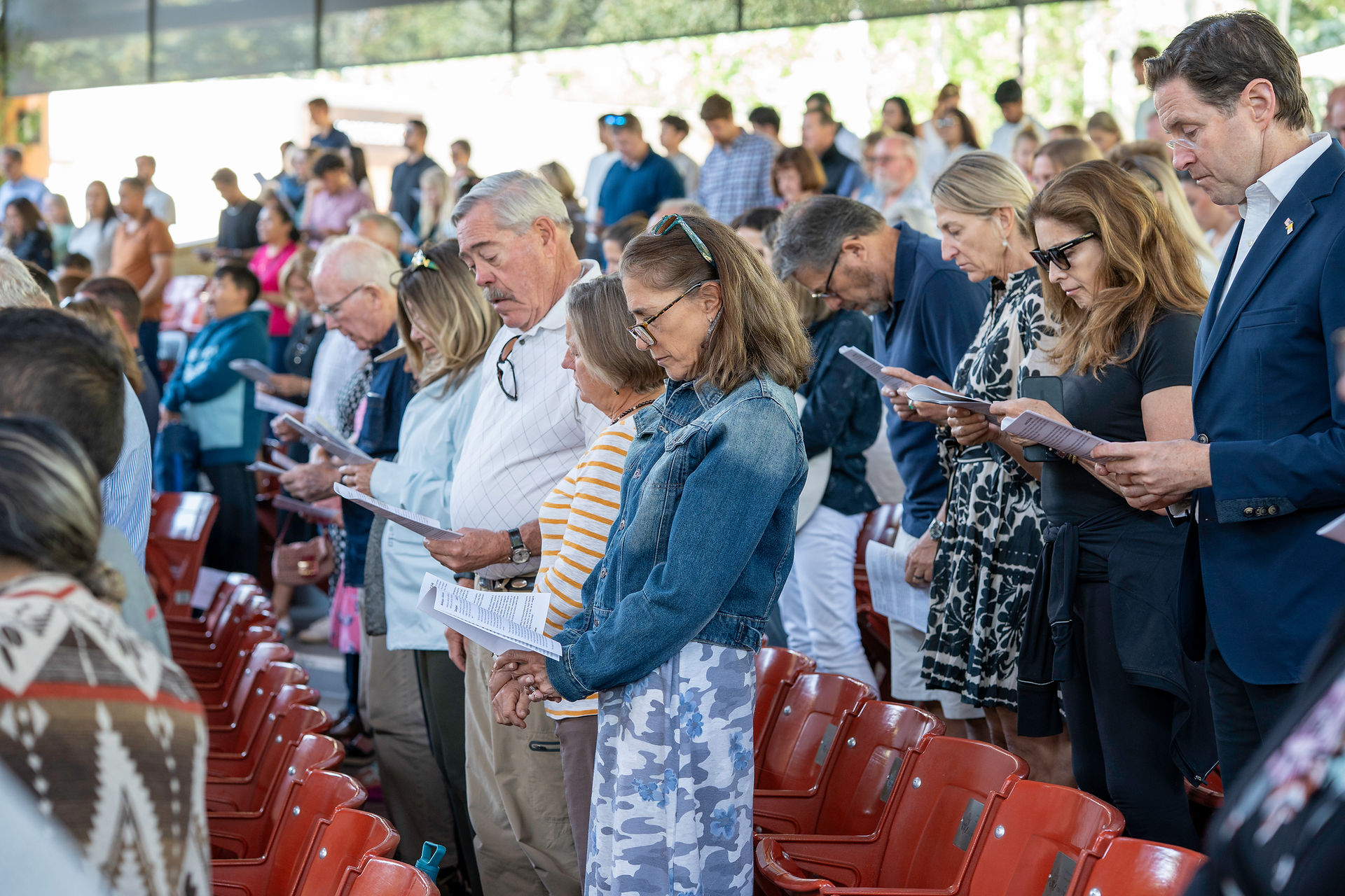 A group of people stand among rows of red seats, holding papers and participating in a ceremony or event.