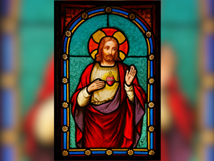 Stained glass of a haloed figure in red and white robes with a sacred heart on the chest, set against a turquoise background with ornate details.
