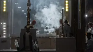 Clergy perform a ritual with incense smoke in a dimly lit cathedral. Ornate altar with white flowers; solemn and reverent atmosphere.