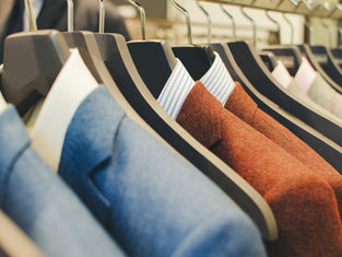Row of suits on hangers, featuring blue and red jackets with striped shirts. Displayed in a retail setting, creating a formal, elegant vibe.