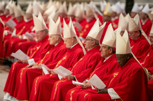 Clergy in red robes and white miters sit in rows, holding papers, in a formal religious setting. The mood is solemn and focused.
