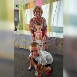 Smiling woman with three children posing indoors under pastel drapes; EXIT sign and shiny silver backdrop behind them.