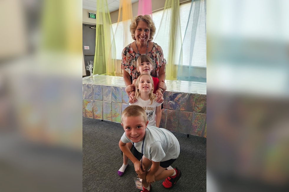 Smiling woman with three children posing indoors under pastel drapes; EXIT sign and shiny silver backdrop behind them.