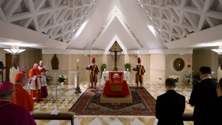 Priests and guards stand by a coffin in a chapel with a triangular ceiling. The scene is solemn with red, gold, and white colors present.