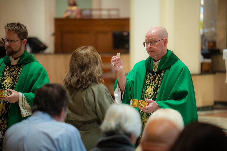 Priests in green vestments distribute communion to worshippers inside a church during a solemn service.