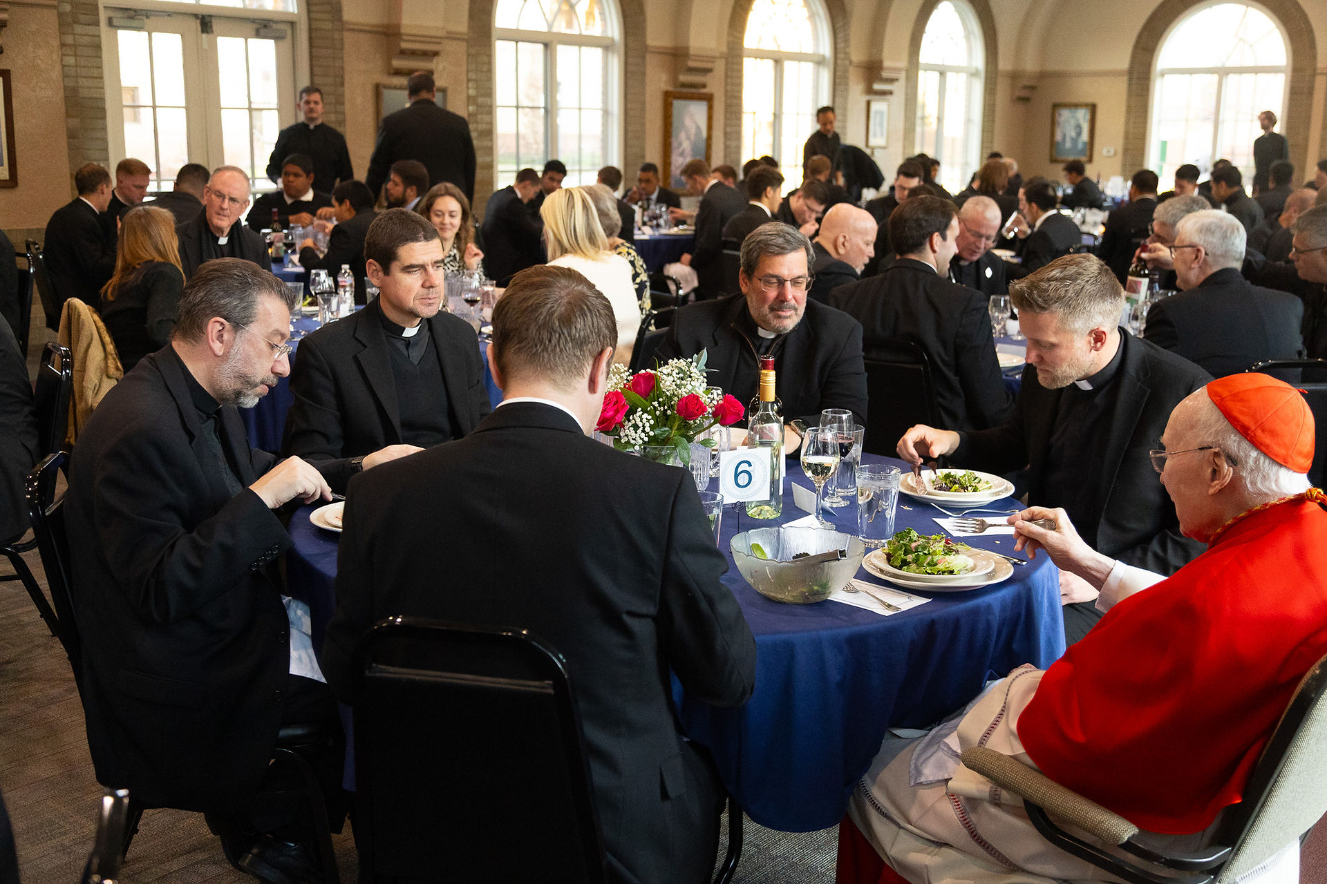 Seminarians and priests at a dinner table with Cardinal Stafford. The mood is celebratory.