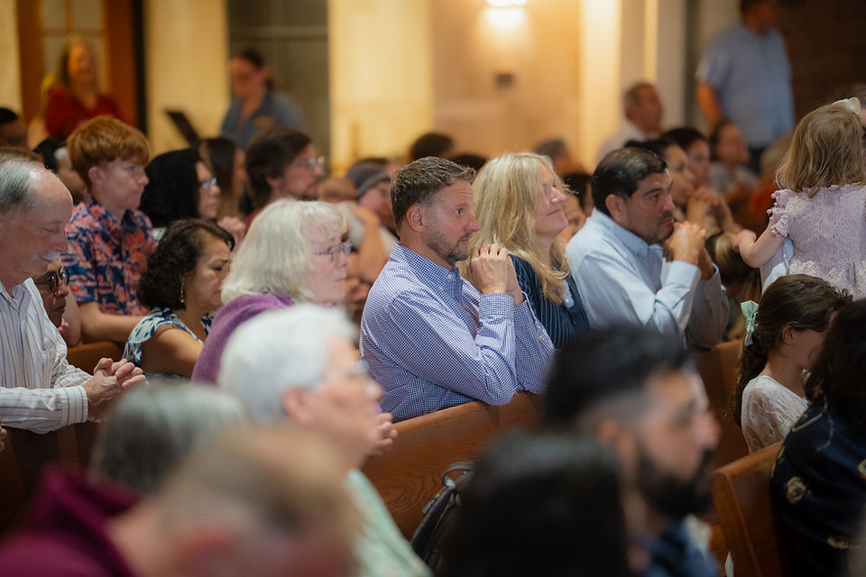 Congregation seated in a warm-lit church, many praying or listening quietly in wooden pews.