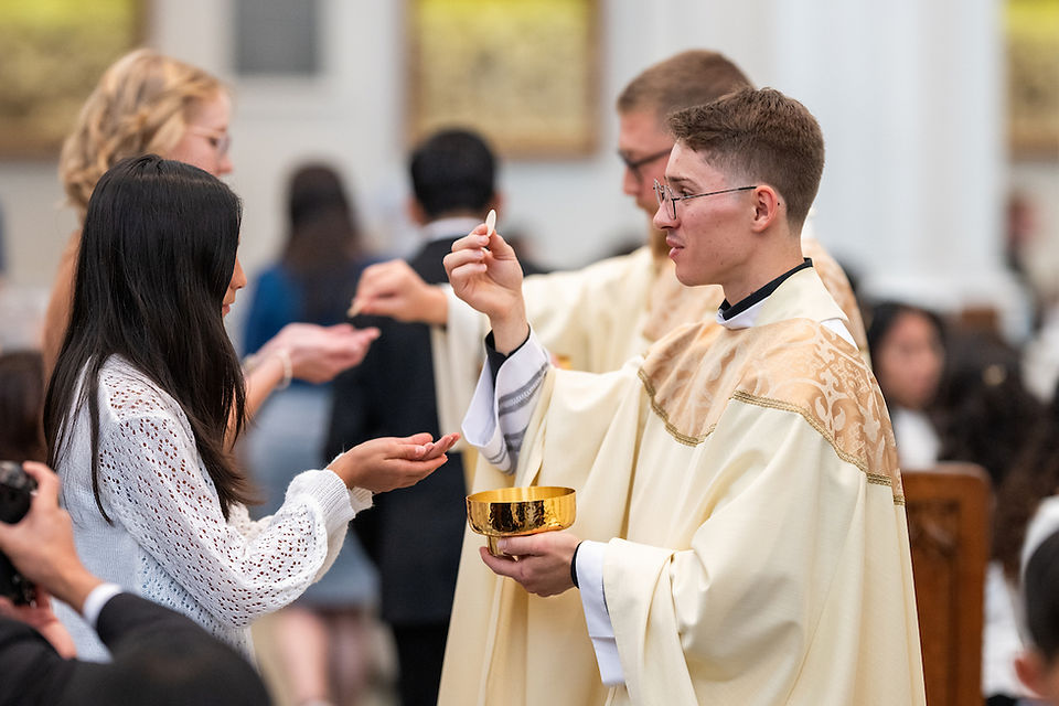 Priest giving communion to a woman in a church setting. He holds a golden chalice. People in the background. Calm and reverent atmosphere.