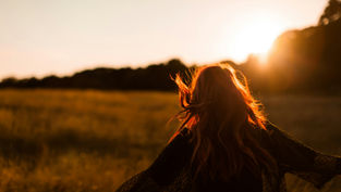 Red-haired person in a field at sunset, running with arms outstretched. Warm golden light and carefree mood.