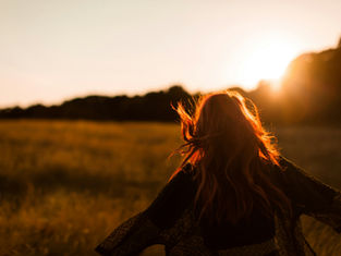 Red-haired person in a field at sunset, running with arms outstretched. Warm golden light and carefree mood.