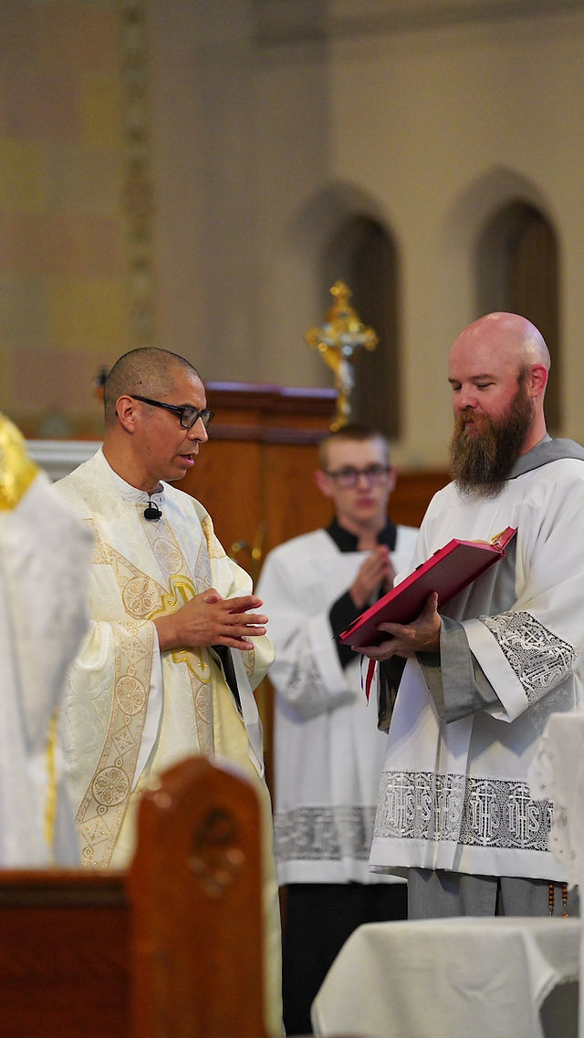 A priest in ornate robes stands in a church, with an altar server holding a red book. A cross is visible in the background, creating a solemn atmosphere.