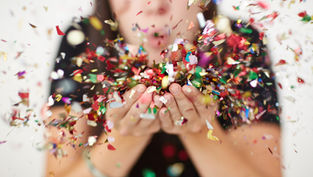 Person blowing colorful confetti from their hands, creating a festive and joyful scene. Blurred background, focus on vibrant confetti.