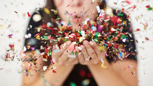 Person blowing colorful confetti from their hands, creating a festive and joyful scene. Blurred background, focus on vibrant confetti.