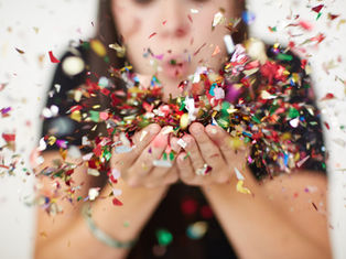 Person blowing colorful confetti from their hands, creating a festive and joyful scene. Blurred background, focus on vibrant confetti.