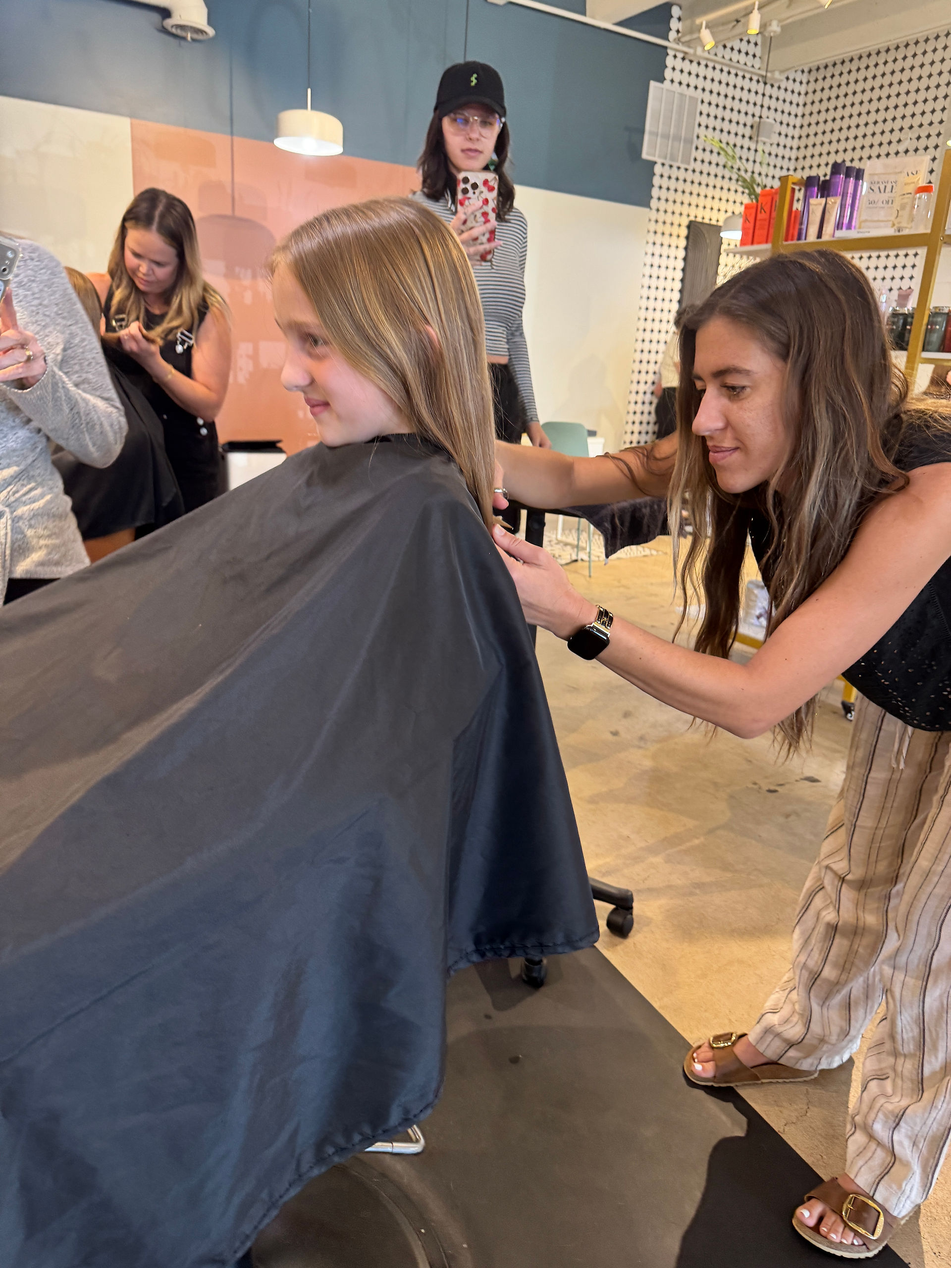 Hair stylist cuts a young girl’s long hair inside a bright salon.