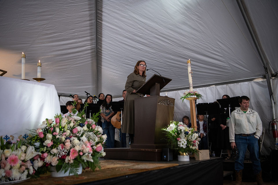A woman speaks from a podium during the groundbreaking ceremony while musicians and attendees listen nearby.