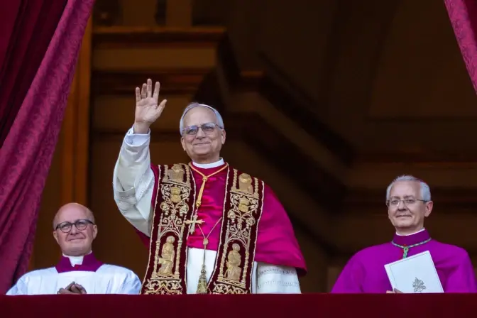 Three clergy in ornate attire stand on a balcony. The central figure waves, displaying a warm smile. Draped curtains frame the scene.