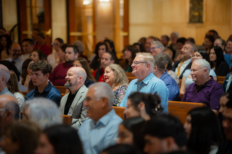 Congregation seated in a warmly lit church, listening attentively and smiling in wooden pews.