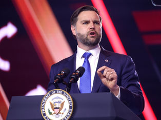 Man in a suit speaks at podium with "Vice President of the United States" seal. Red and orange lights in the background. Determined expression.
