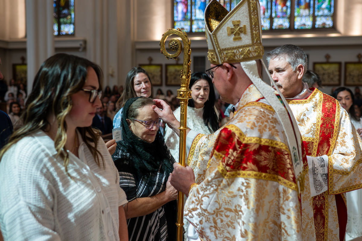 A bishop blesses a woman as she bows her head among a group of parishioners.