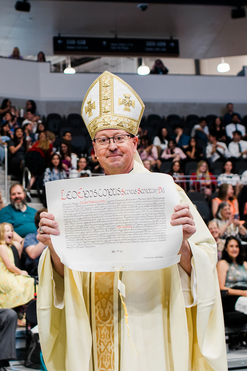 A newly installed bishop holds up an apostolic mandate as the congregation looks on.